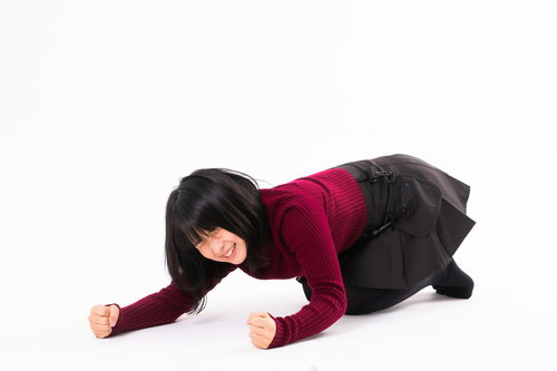 赤いトップスを着て床に両手を打ち付けて悔しがる女性