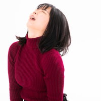 赤いニットセーターを着て天を仰いで後悔する女性の写真