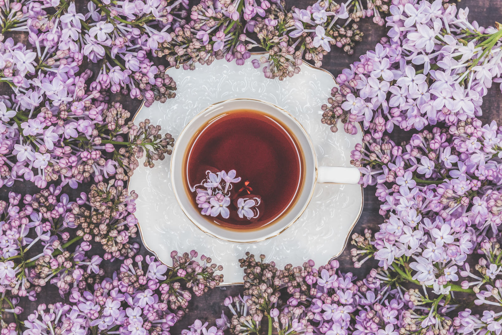 ライラックの花に囲まれた紅茶入りの白いティーカップ