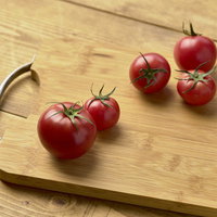 木目のまな板に並ぶ赤いミニトマト、ヘタ付きの写真