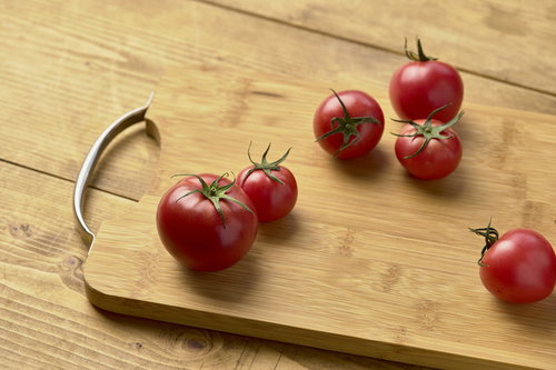 木目のまな板に並ぶ赤いミニトマト、ヘタ付き