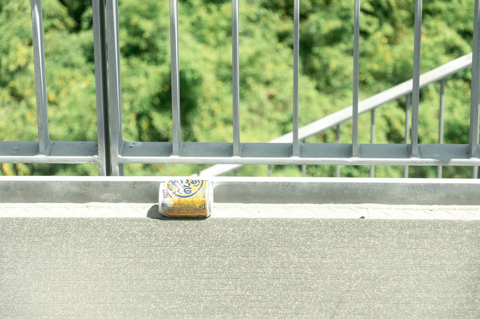 グレーの手すりの上に置かれた金色のビール缶と背景の緑の植物
