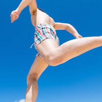 青空に向かってジャンプする海パン姿の男性の写真