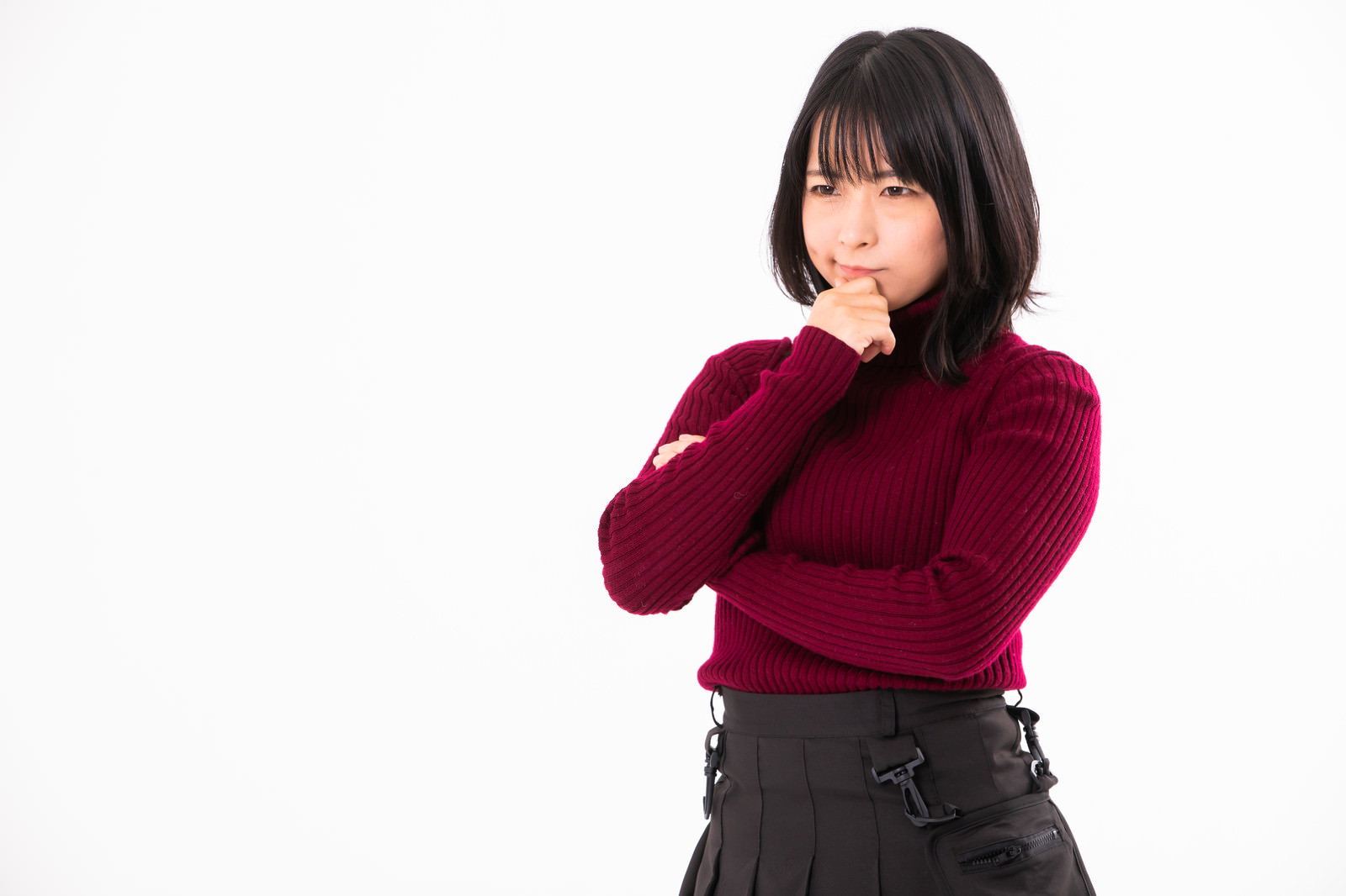 顎に手を当てて考える表情をする赤いセーターの女性［モデル：にゃるる］