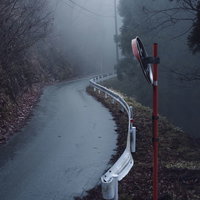 朝霧に包まれた林道に立つカーブミラーとガードレールの写真