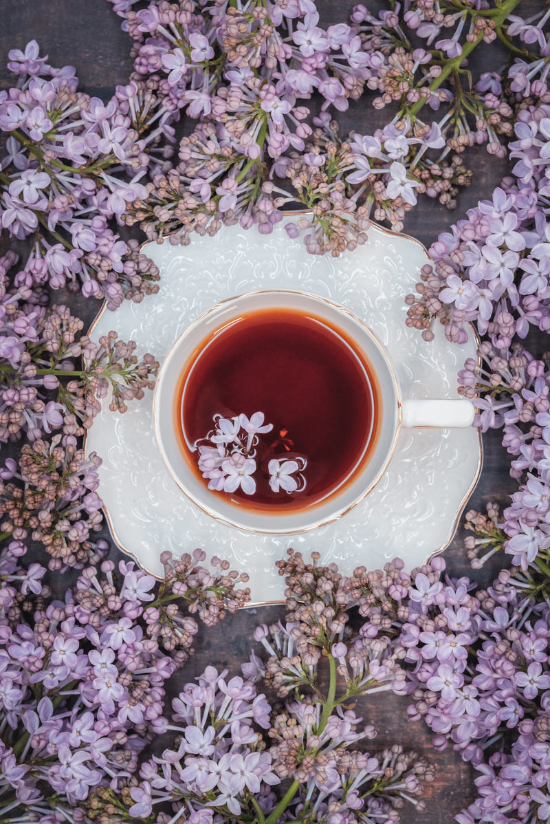 白いティーカップに入った紅茶の表面に浮かぶ紫色のライラックの花びら