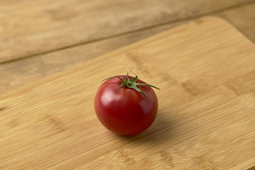 木目のまな板に置かれた蔕付きミニトマトの鮮やかな赤色