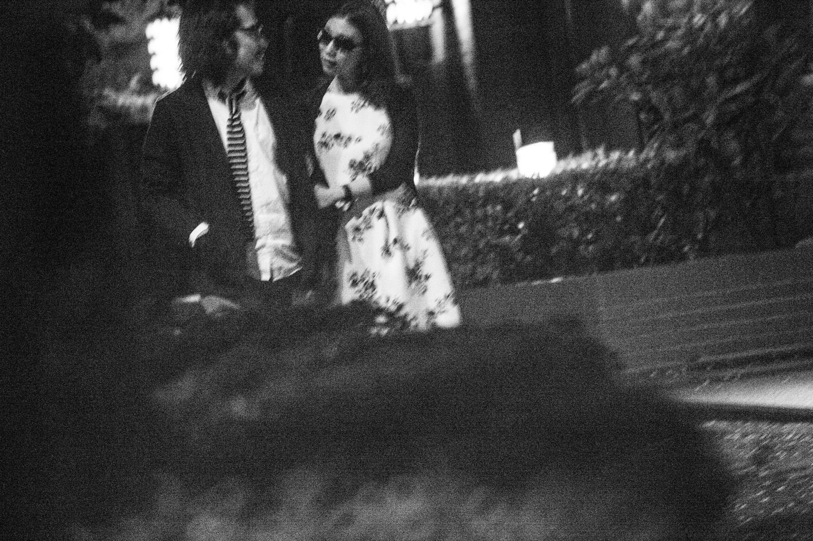 夜の路上で向き合って会話するスーツの男性と花柄ブラウスの女性［モデル：ゆうせい］