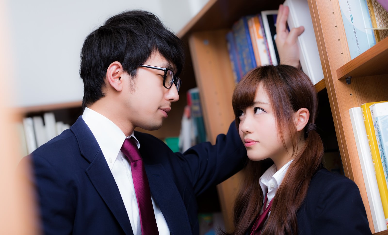 図書室で本棚を背景に制服の男女が向き合っている［モデル：大川竜弥 河村友歌］