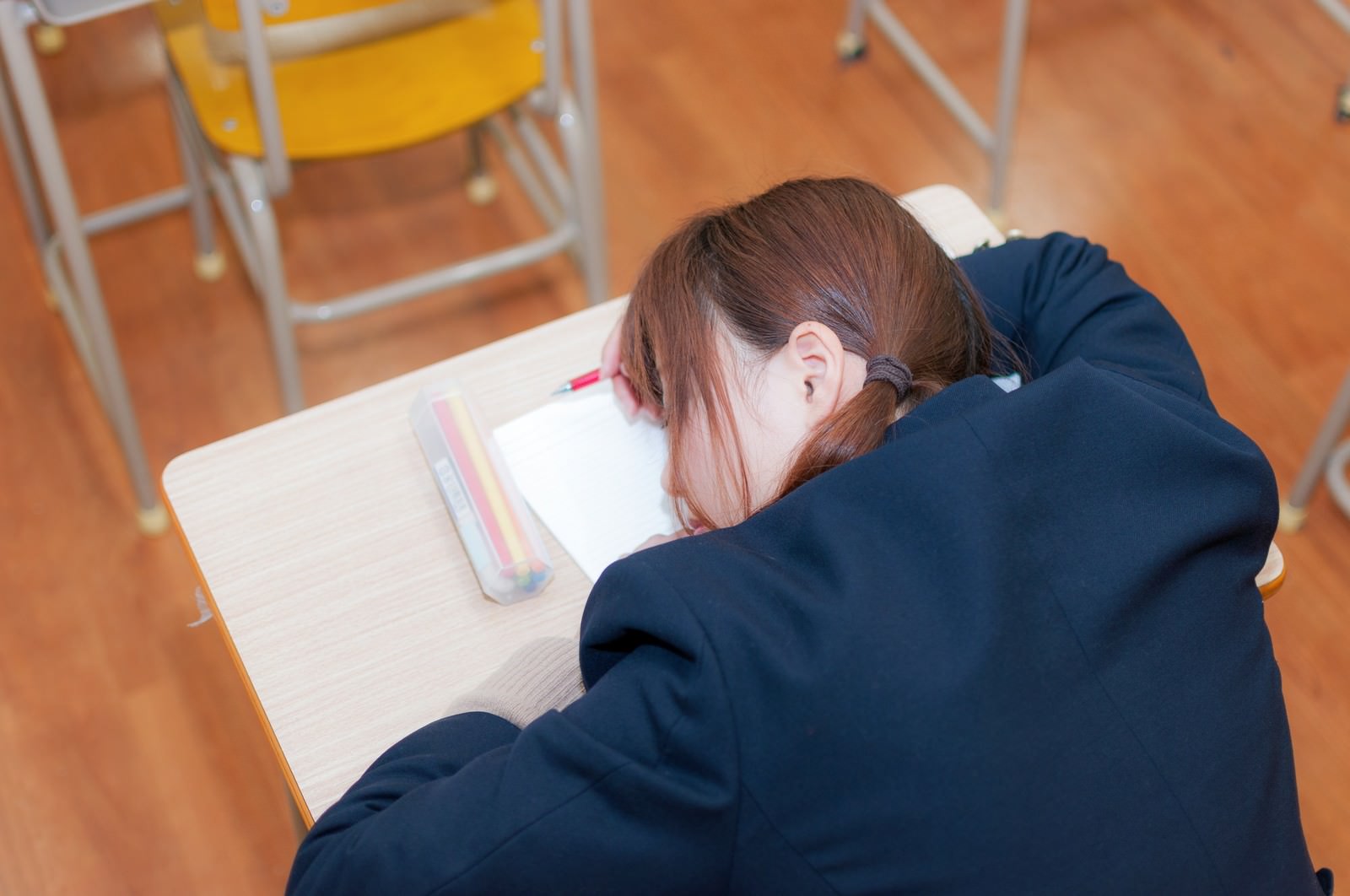 勉強中に机でうつぶせに寝ている紺色の制服を着た女子高生［モデル：河村友歌］