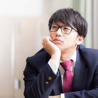 推理に行き詰まる眼鏡の男子高校生が頬杖をついて考え込むの写真