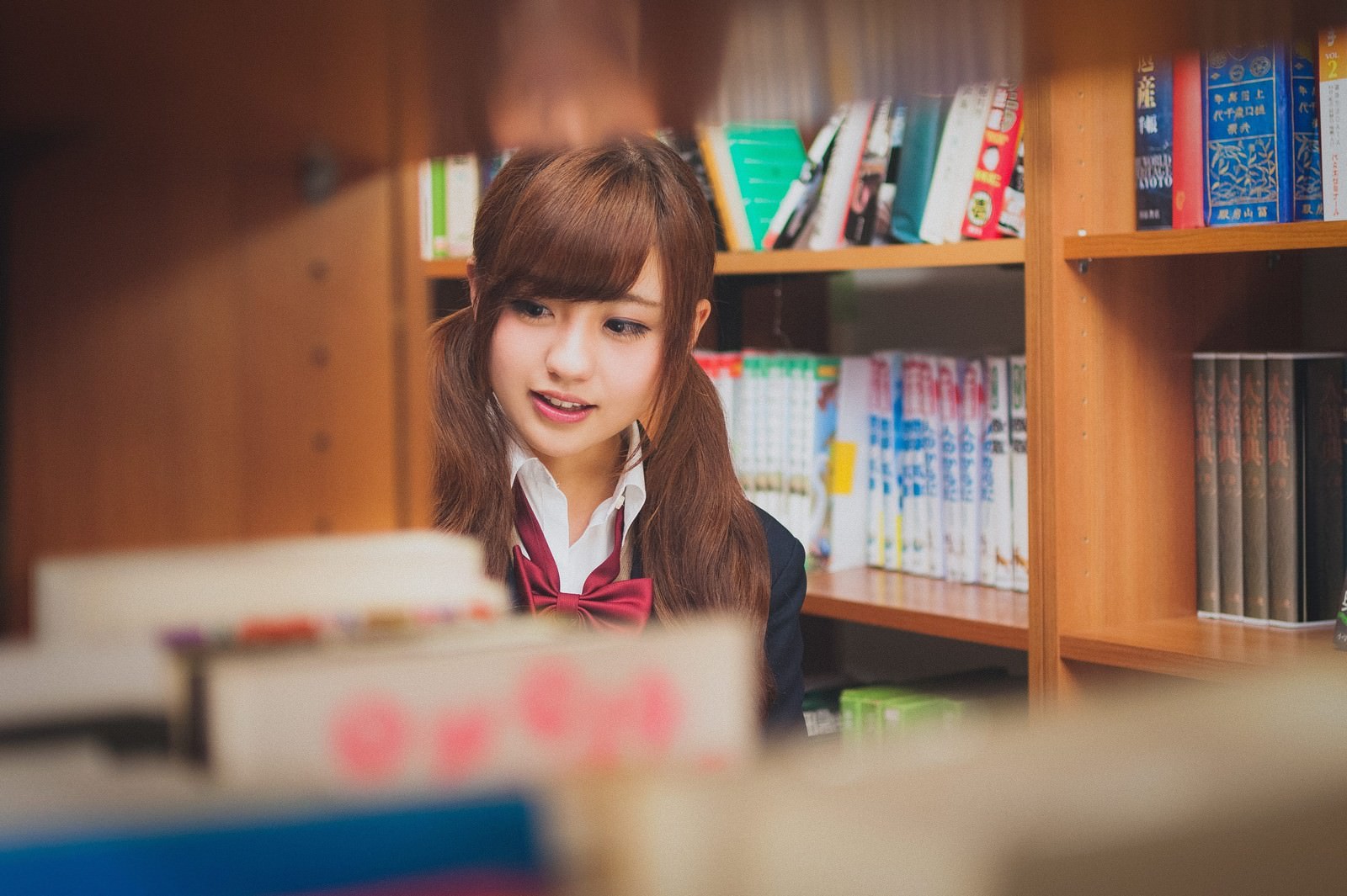 図書室で読書する赤いリボンの制服姿の女子高生［モデル：河村友歌］