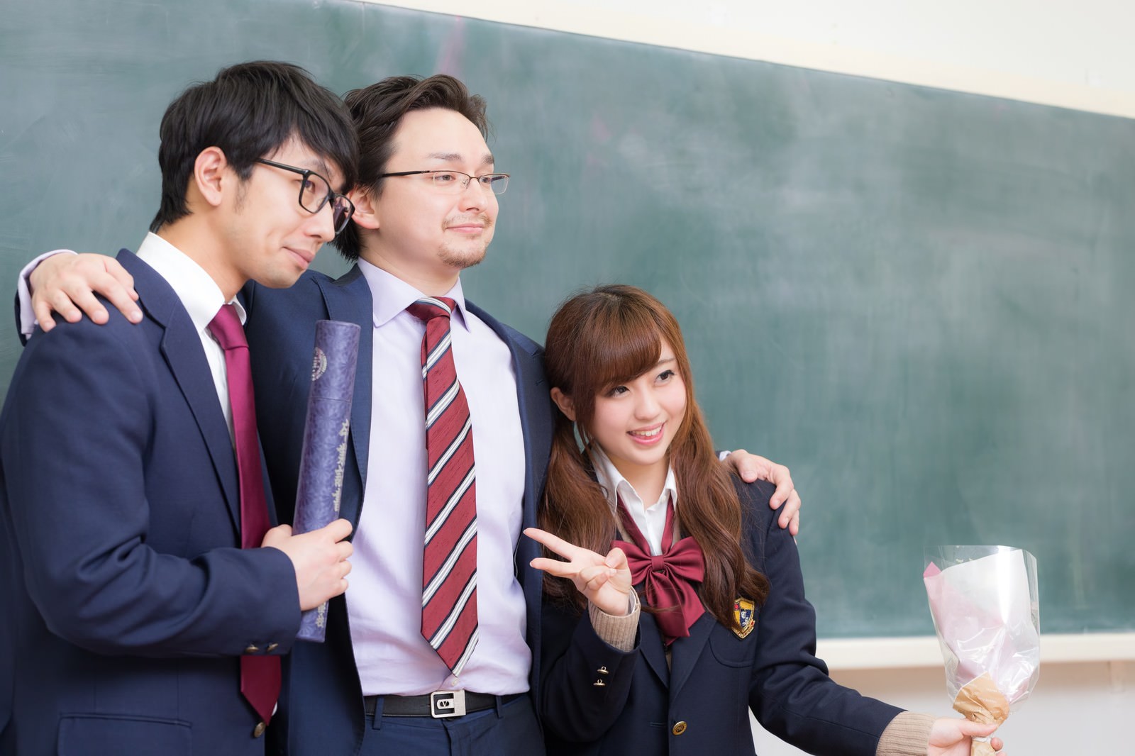 卒業式の後、黒板の前で肩を寄せ合って笑顔で記念撮影をする教師と女子高生、男子高生［モデル：大川竜弥 Max_Ezaki 河村友歌］
