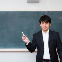 黒板の前でチョークを持ち授業をする新任教師の写真