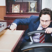 校長室の机で書類をチェックするハイスクール用務員の写真