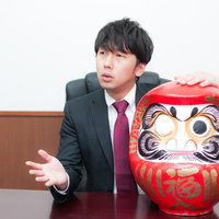 取材にこたえる役員と片目の達磨、選挙必勝祈願の写真