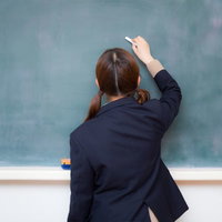 黒板にチョークで文字を書く制服姿の女子高生の写真