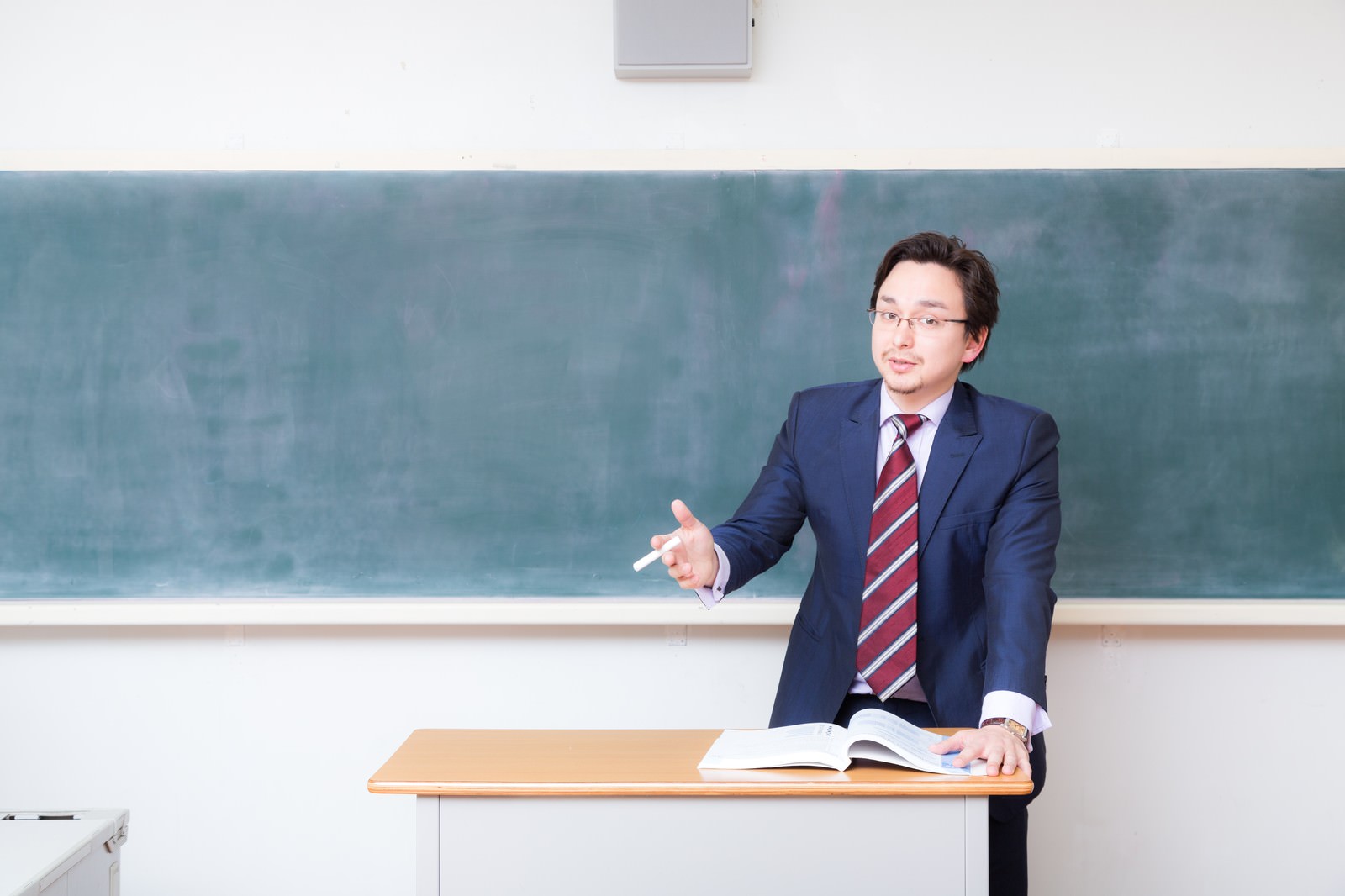 黒板の前でドイツ語の授業を行うスーツ姿の男性教師［モデル：Max_Ezaki］