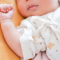 ぐっすり眠る新生児の寝顔、親の腕に抱かれて安心した表情の写真