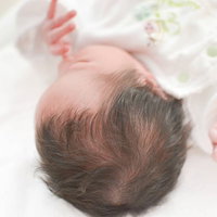 白いベッドの上で指をしゃぶる新生児の赤ちゃんの写真