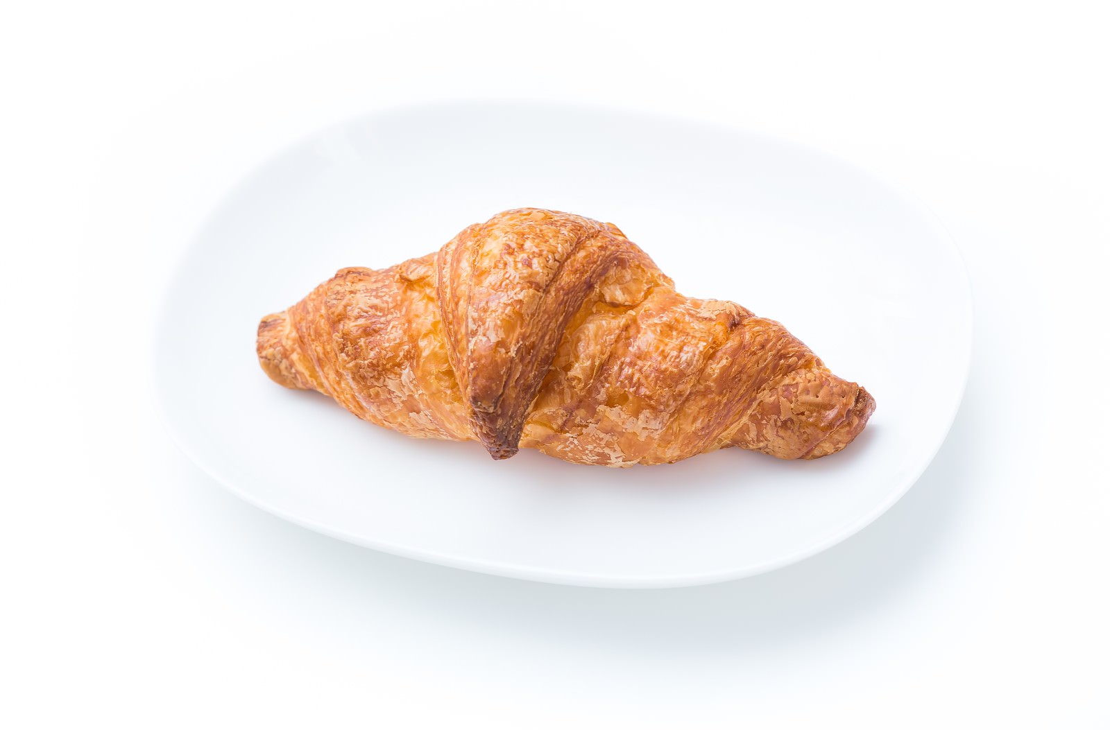 白いお皿に置いたクロワッサン。焼き色のついた層状のパンで、表面に光沢がある