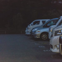 夜間の不気味な駐車場に並ぶ車列と懐中電灯の光の写真