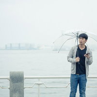 雨の日の待ち合わせで傘を持つ男性がスマートフォンを確認の写真