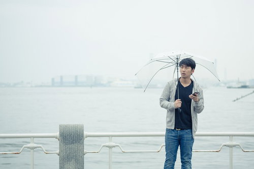 雨の日の待ち合わせで傘を持つ男性がスマートフォンを確認