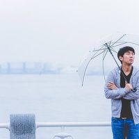 雨の中、傘を持って空を見上げる若手俳優の横顔の写真