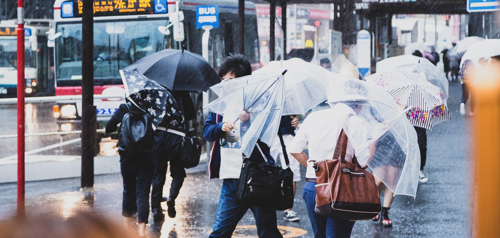 駅前で横なぐりの雨に対抗する複数の人物と傘