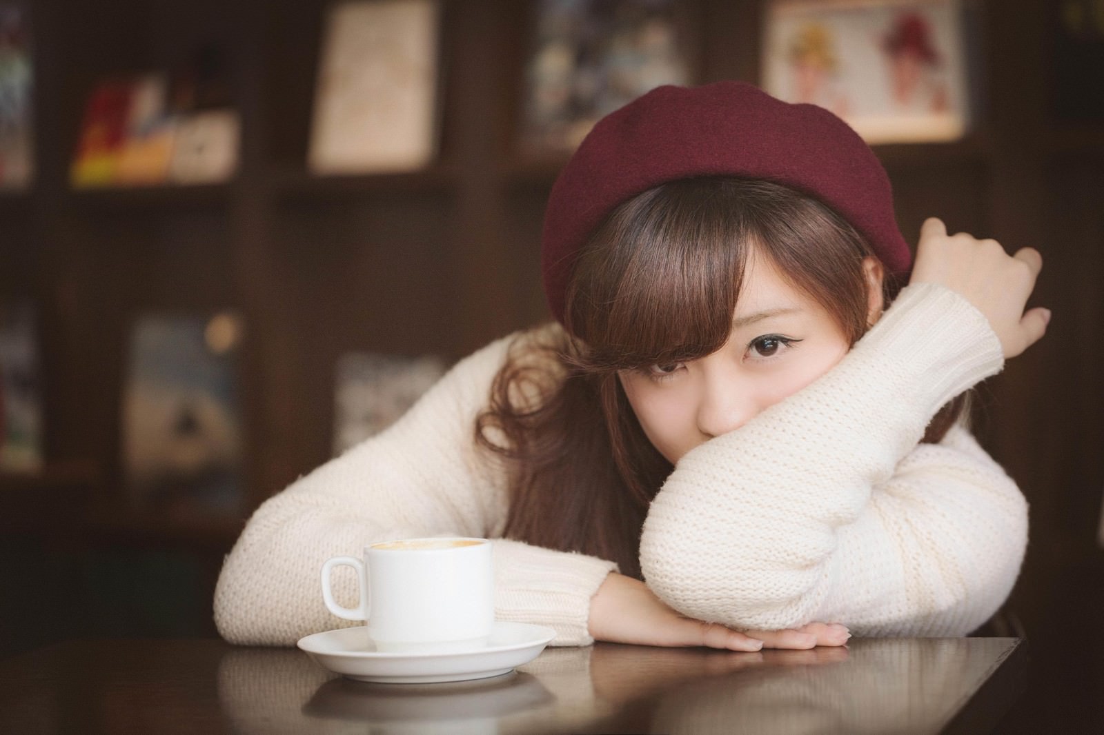 カフェでカップの前に肘をついて俯く、白いニット姿の女性［モデル：河村友歌］