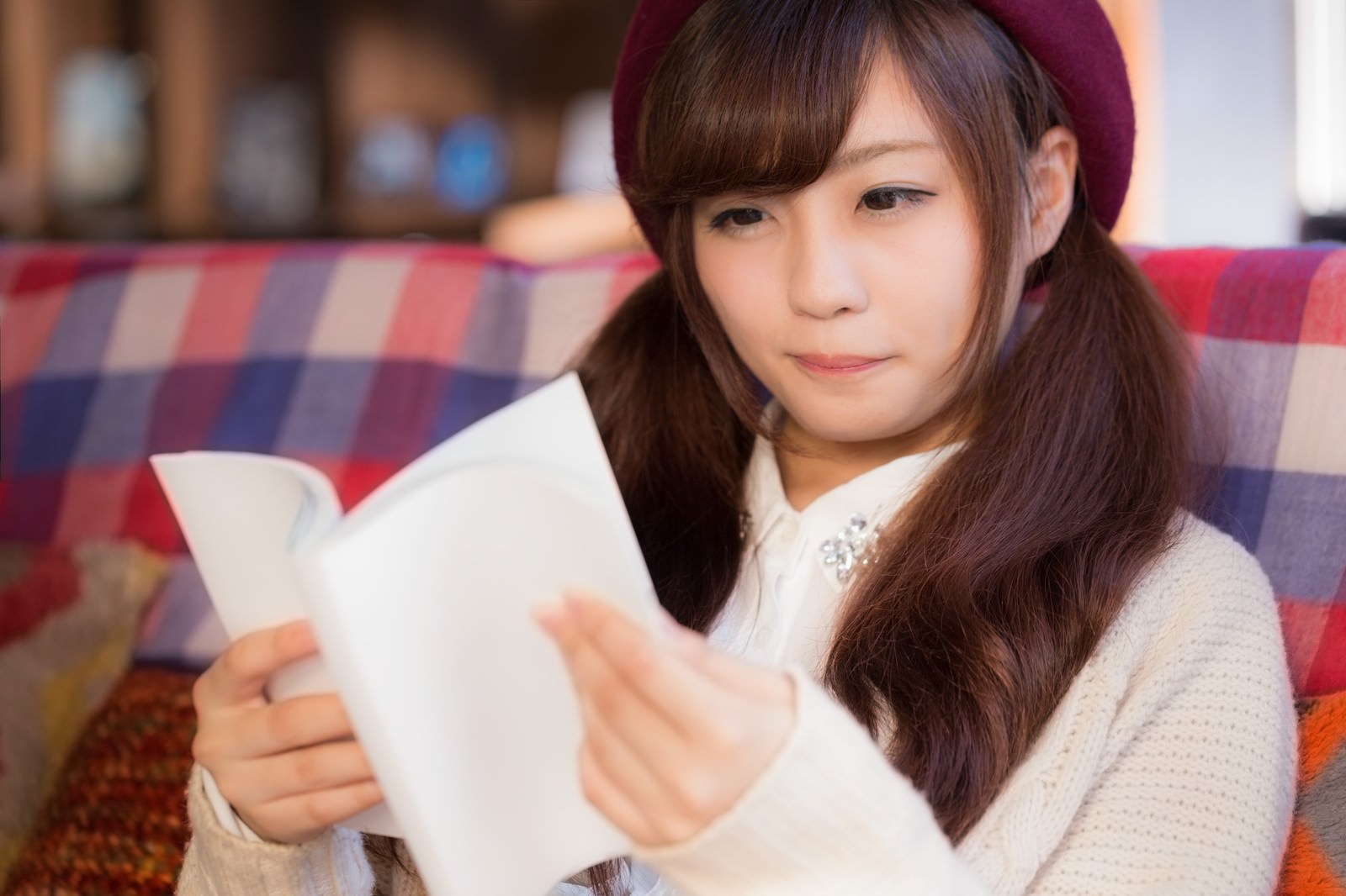ソファーに座りながら雑誌を読むベレー帽姿の女性［モデル：河村友歌］