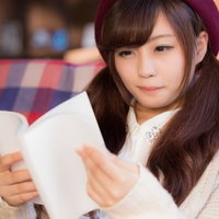 新刊の雑誌をソファーで読むベレー帽の女性の写真