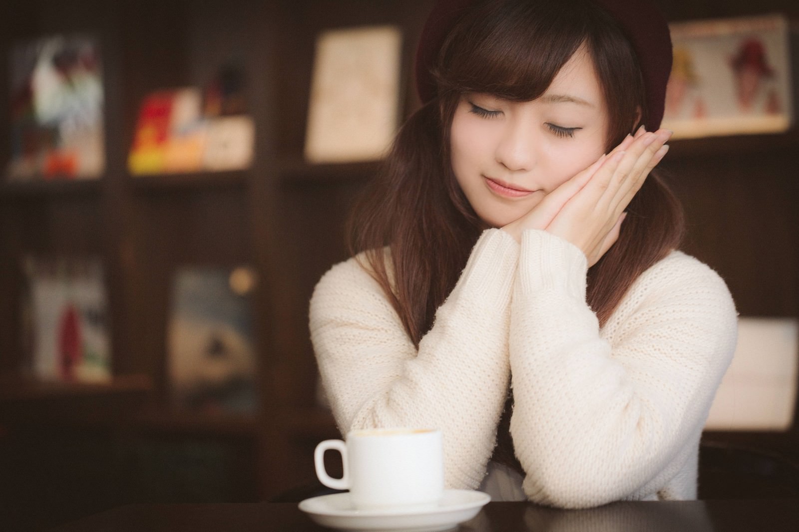 カフェで手を頬に当てて目を閉じる白いセーター姿の女性［モデル：河村友歌］