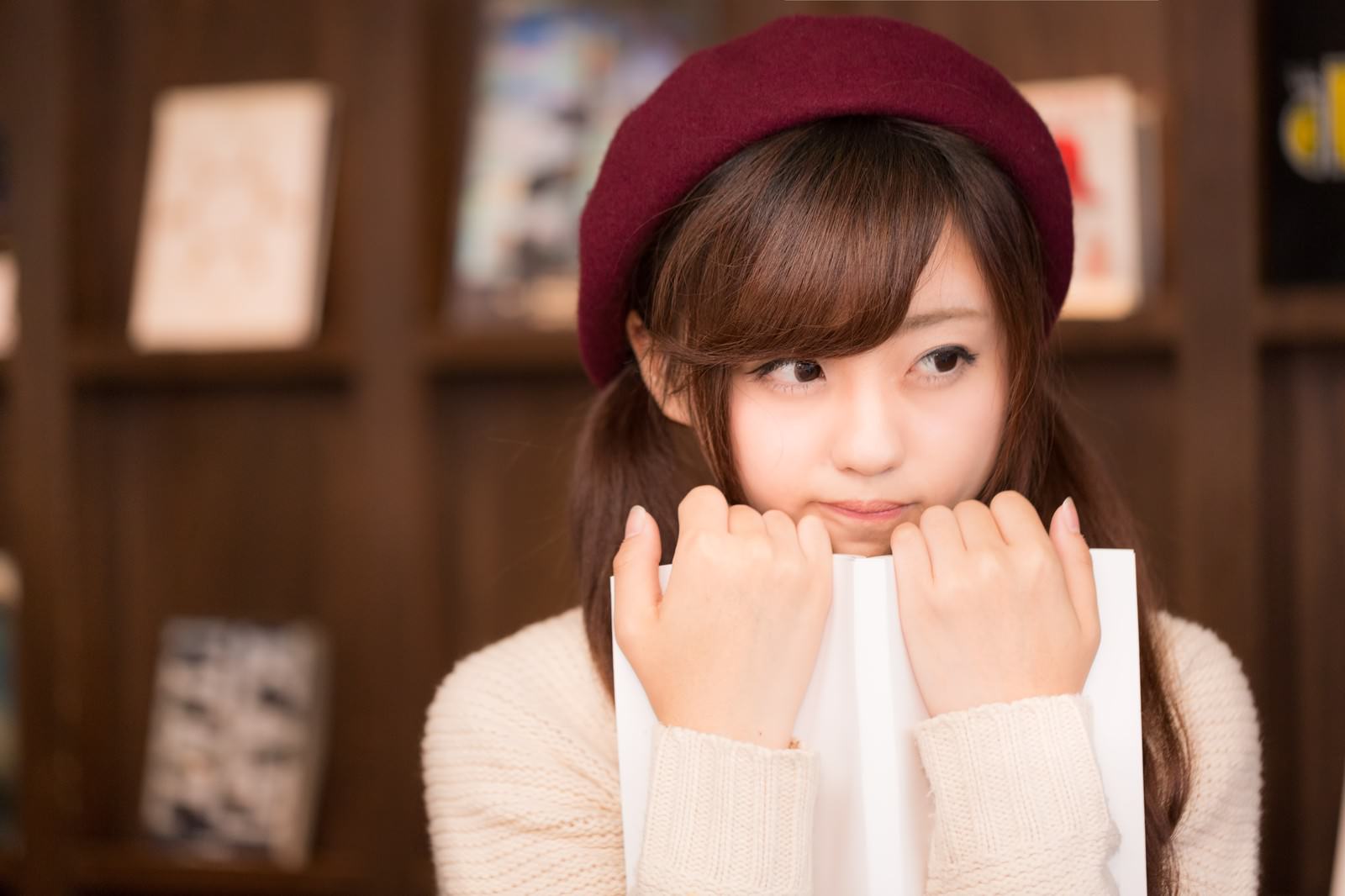 えんじ色のベレー帽をかぶった女性が本を胸に抱きしめ、感動して涙ぐむ［モデル：河村友歌］