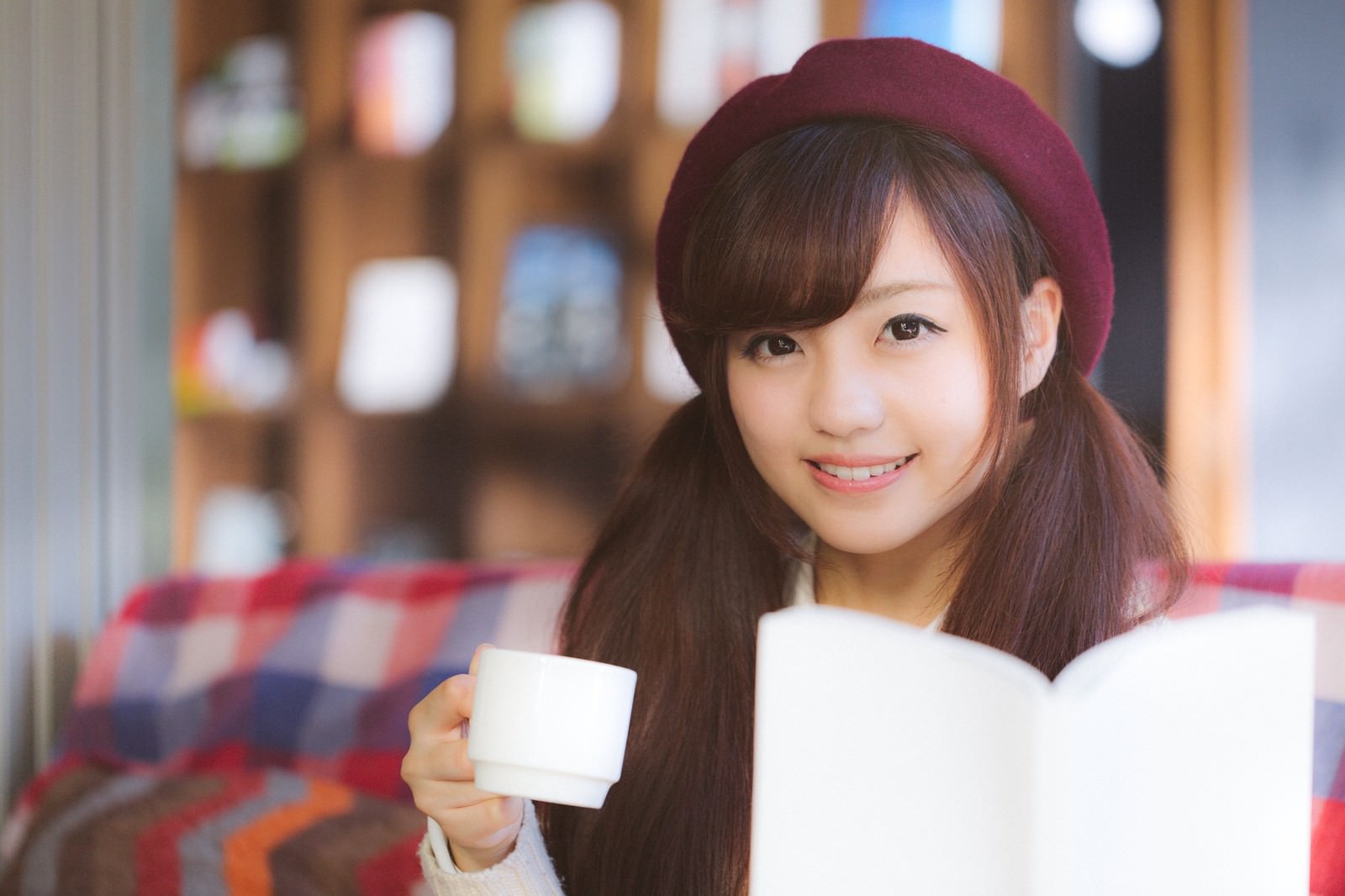 カフェで本を読みながら微笑む女性［モデル：河村友歌］