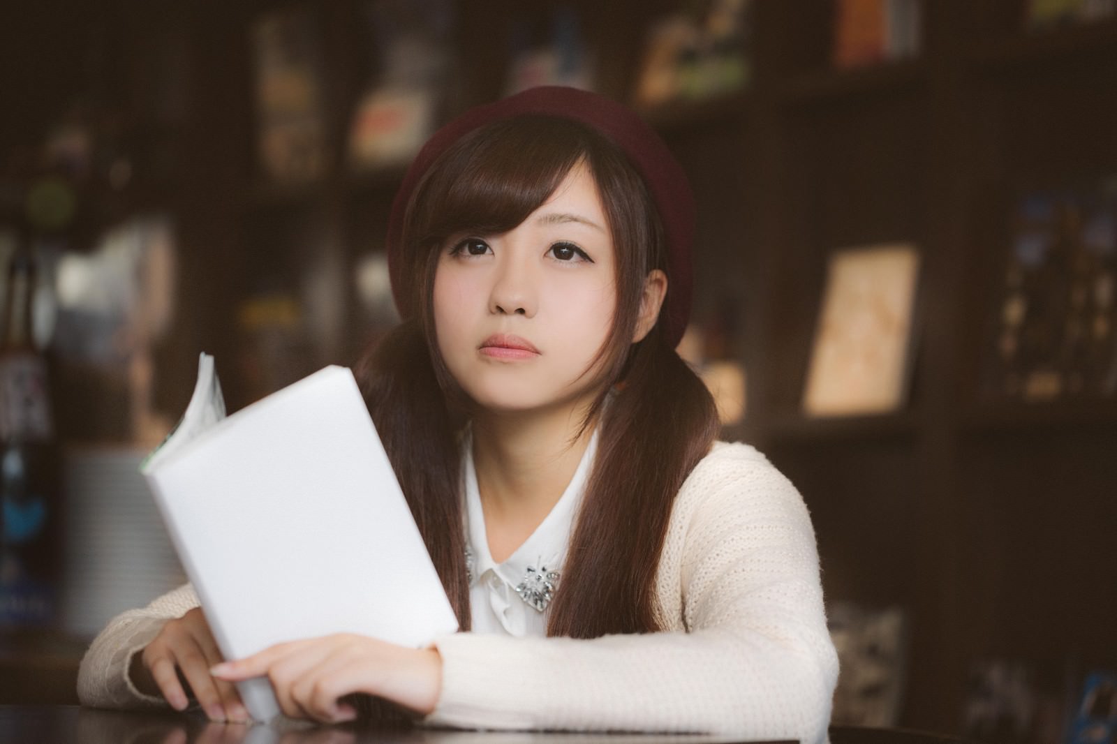 マンガを手に持ち遠くを見つめるベレー帽とカーディガン姿の女性［モデル：河村友歌］