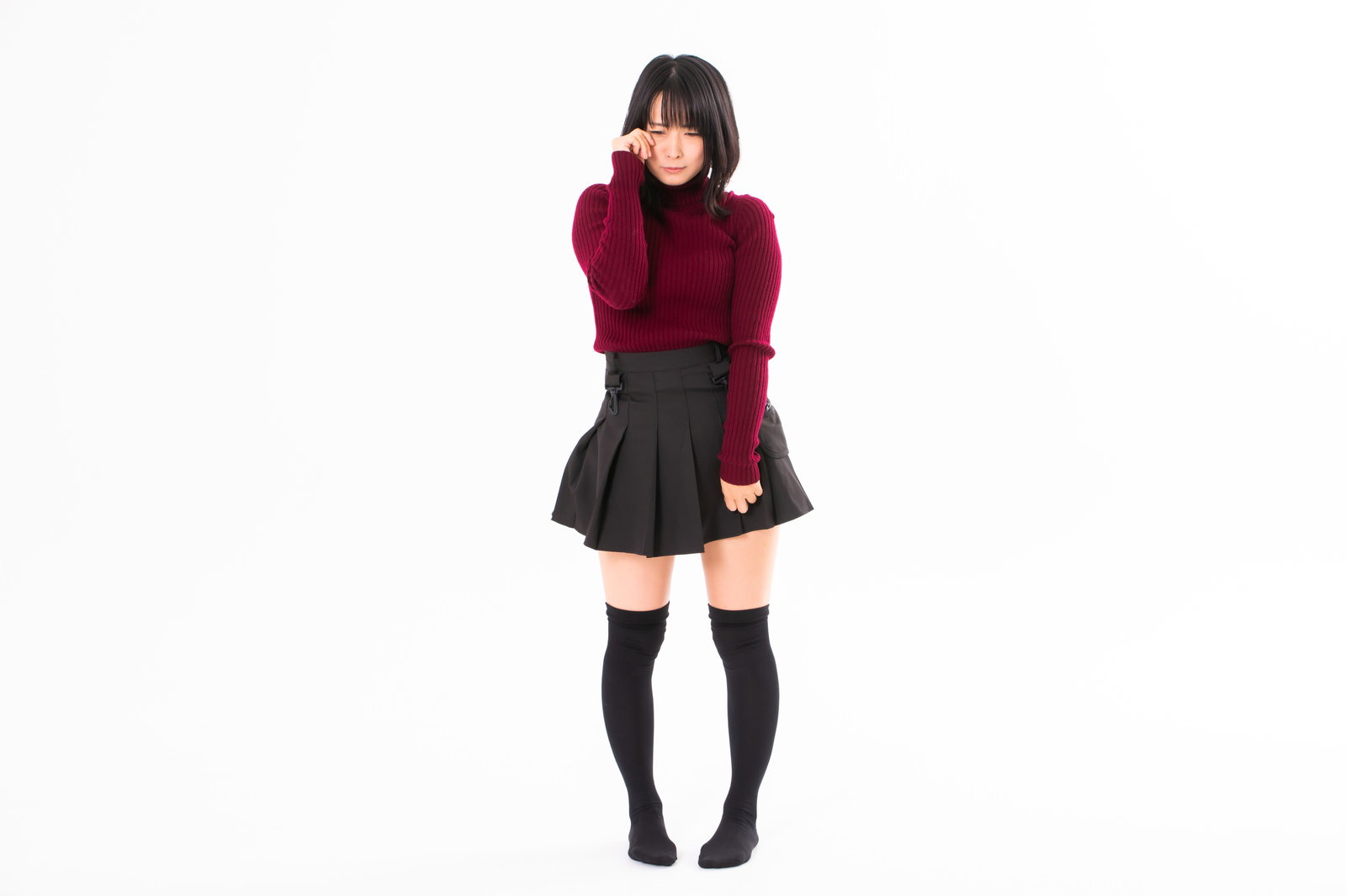 赤いニットと黒いスカートを着た女性が両手で顔を覆って泣いているポーズ［モデル：にゃるる］
