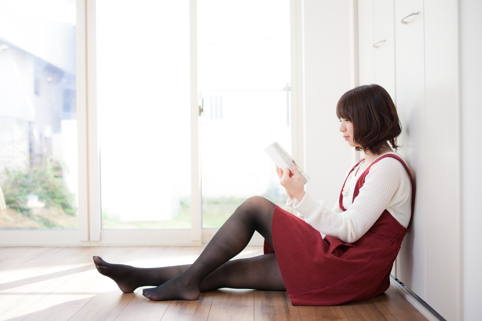 窓際で漫画を読む赤いベストを着た女性の横顔［モデル：みき。］