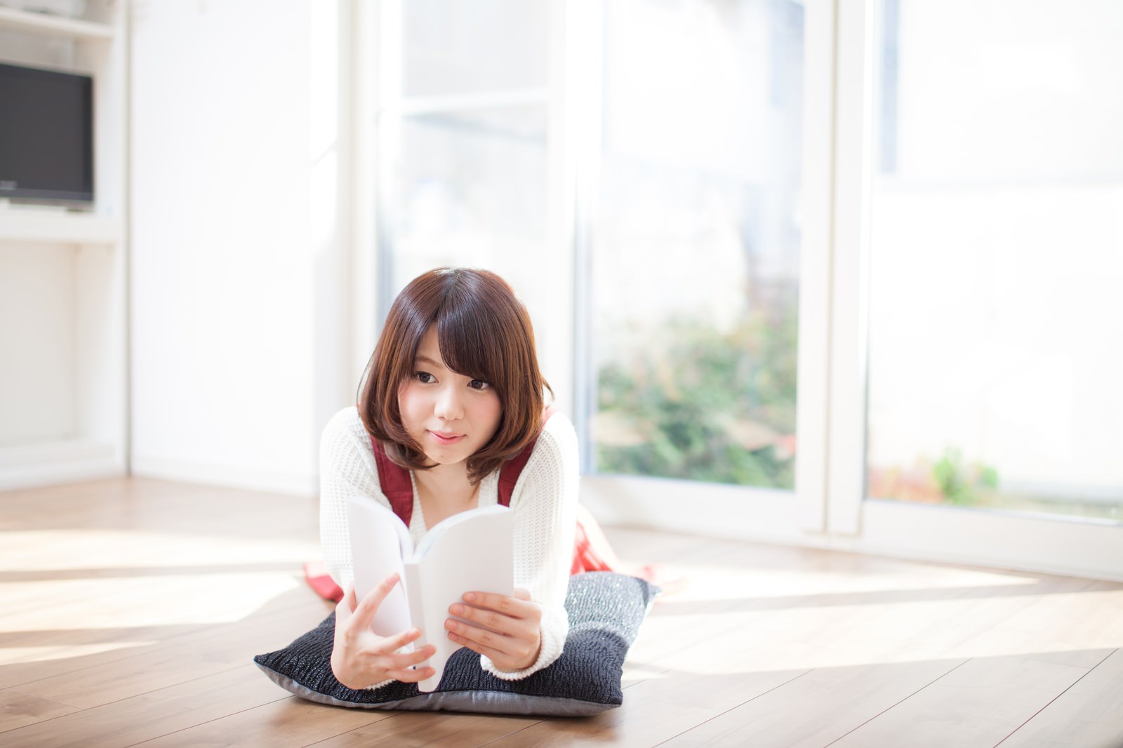 リビングのフローリングに座ってマンガを読む女性［モデル：みき。］