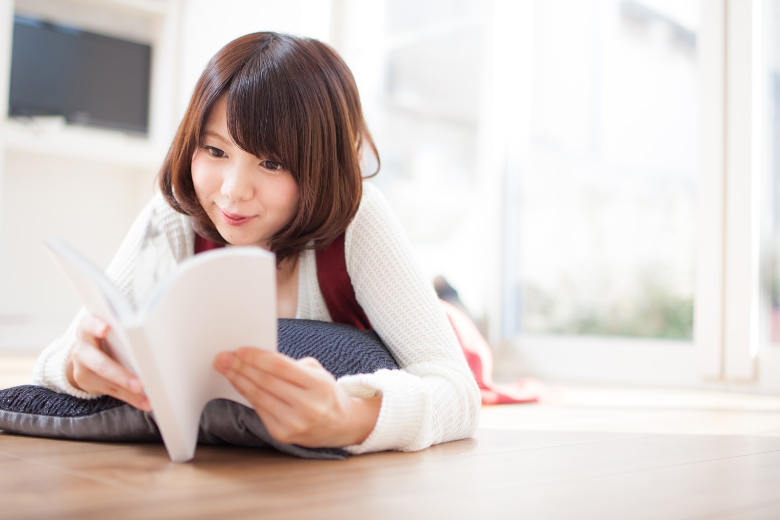 マンガを読む女性がフローリングで寝転んで笑っている［モデル：みき。］