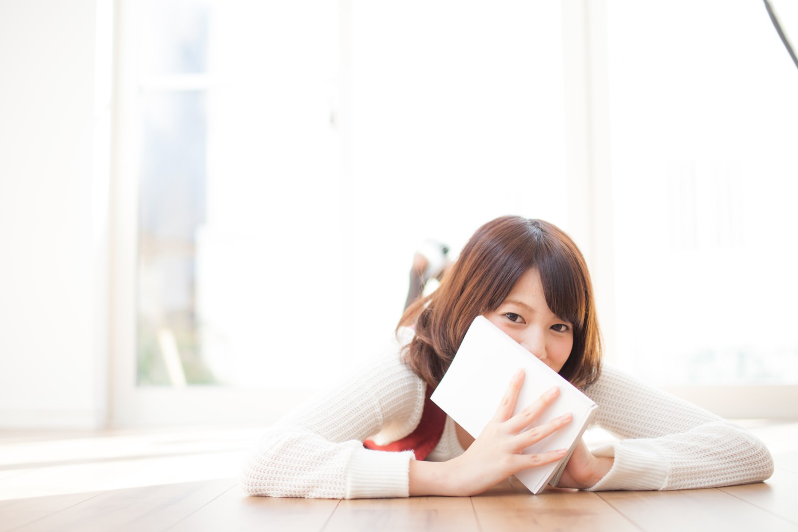 本で顔を隠しながら照れ笑いする読書中の女性［モデル：みき。］