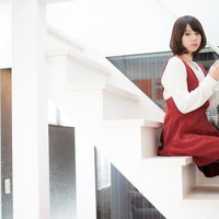階段に座って本を読む女性、白いニットカーディガンと赤いワンピース姿の写真