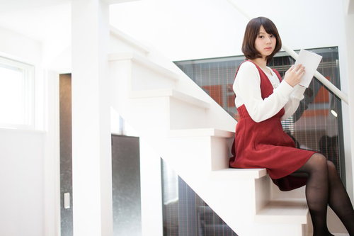 階段に座って本を読む女性、白いニットカーディガンと赤いワンピース姿
