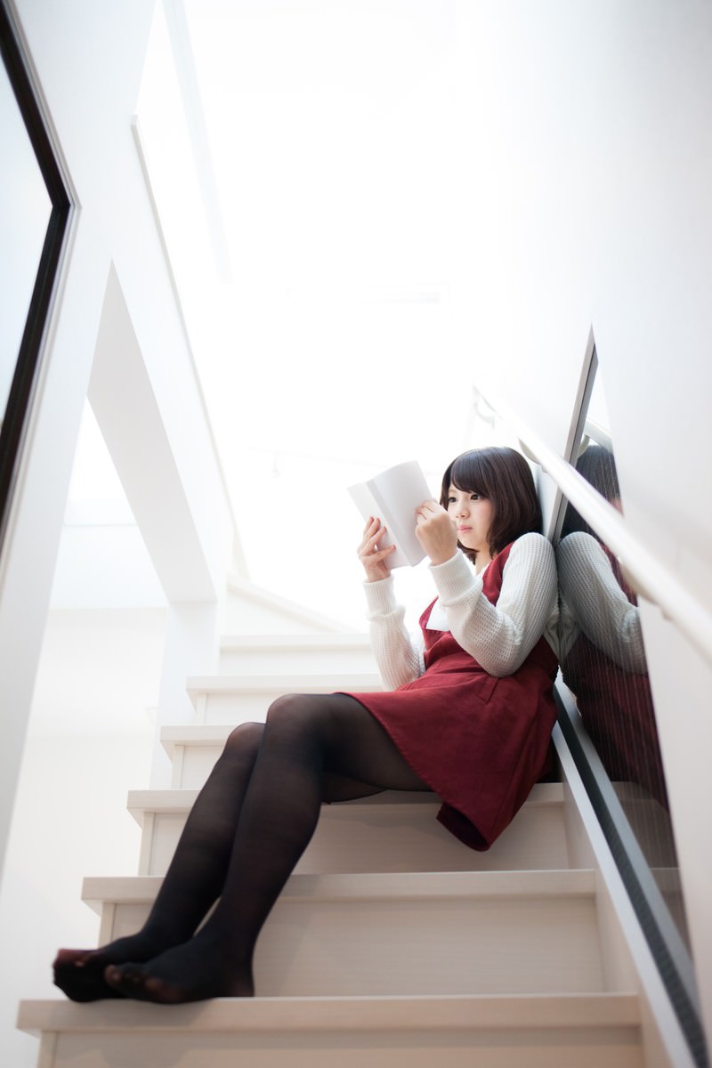 階段に座ってタブレットで漫画を読む赤いワンピースの女性［モデル：みき。］