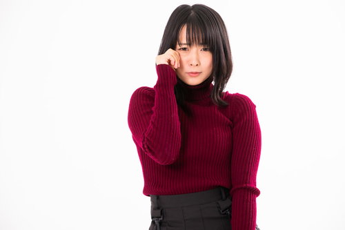 赤いニットセーターを着た女性が手で顔を覆うウソ泣きポーズ