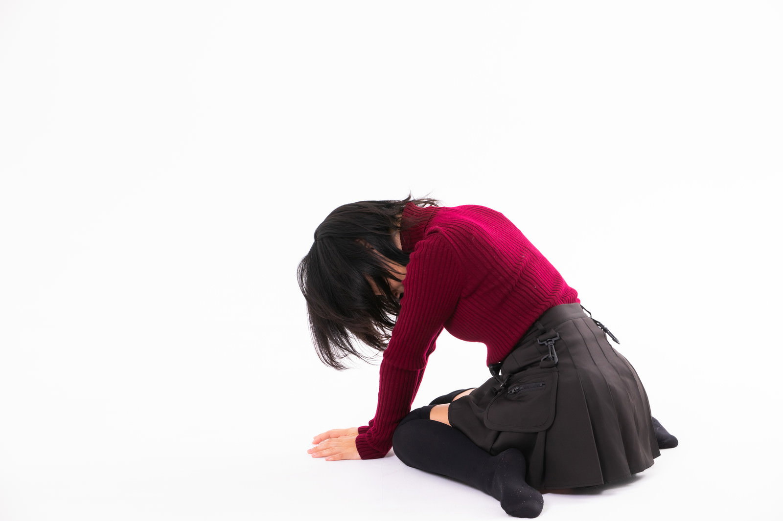 赤いトップスを着た女性が膝をついて深くうなだれている［モデル：にゃるる］