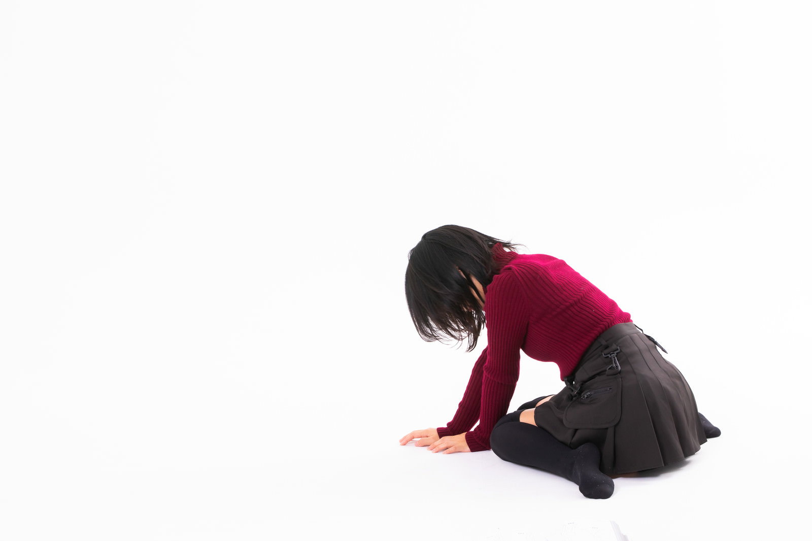落ち込んで座り込む女性、赤いトップスを着て床に膝をついてうつむいている［モデル：にゃるる］