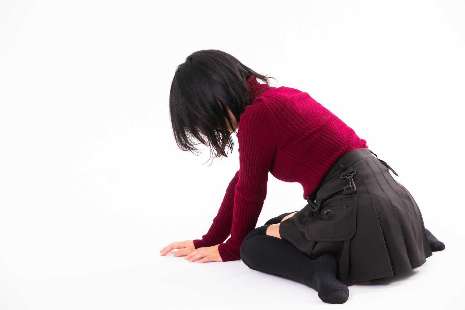 深紅のセーターを着た女性が床に膝をつき落ち込んでいる様子［モデル：にゃるる］