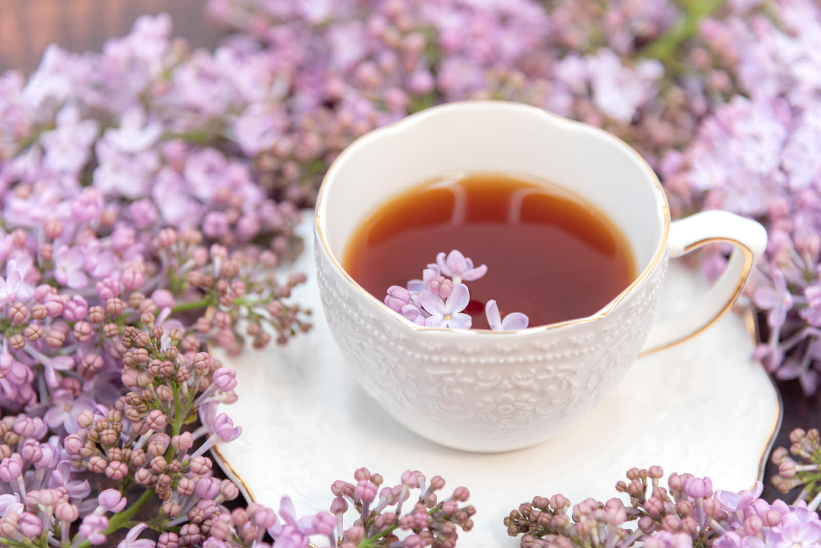 紫色のライラックの花に囲まれた白いティーカップと紅茶
